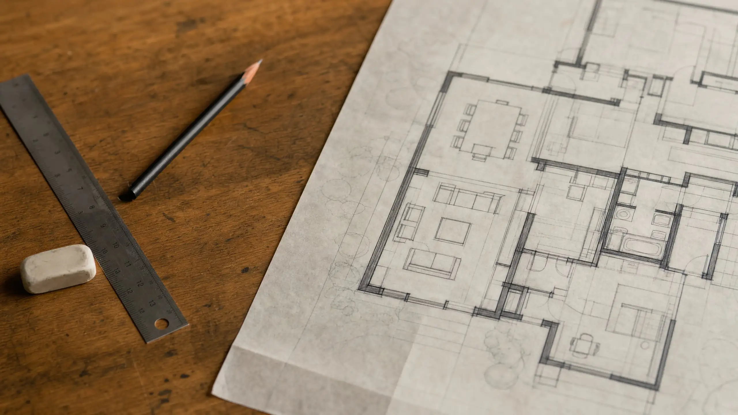 Hand-drawn addition floor plan with furniture layout, a scale ruler and pencil on a drafting table