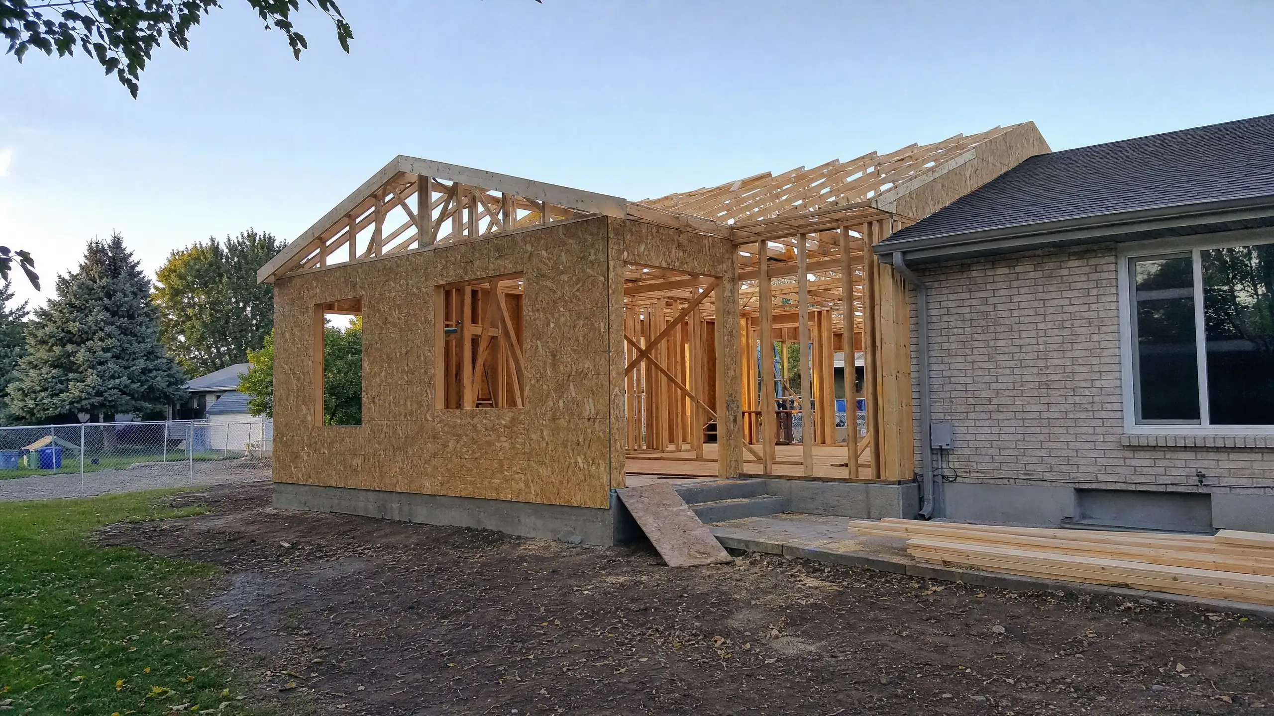 Home addition under construction with roof trusses and wall sheathing tied into an existing rambler
