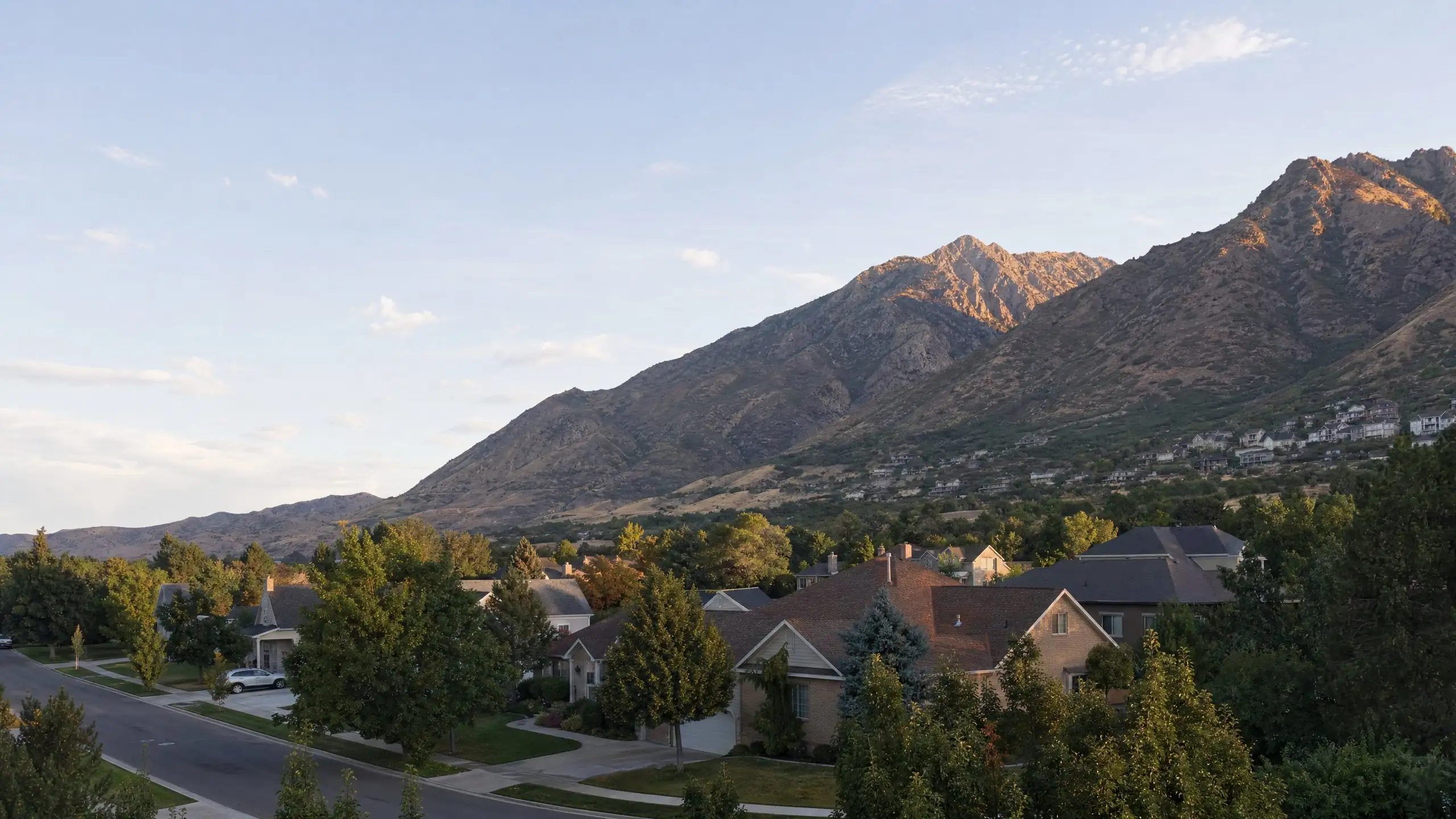 Suburban neighborhood with tree-lined streets at the base of the Wasatch foothills in evening light