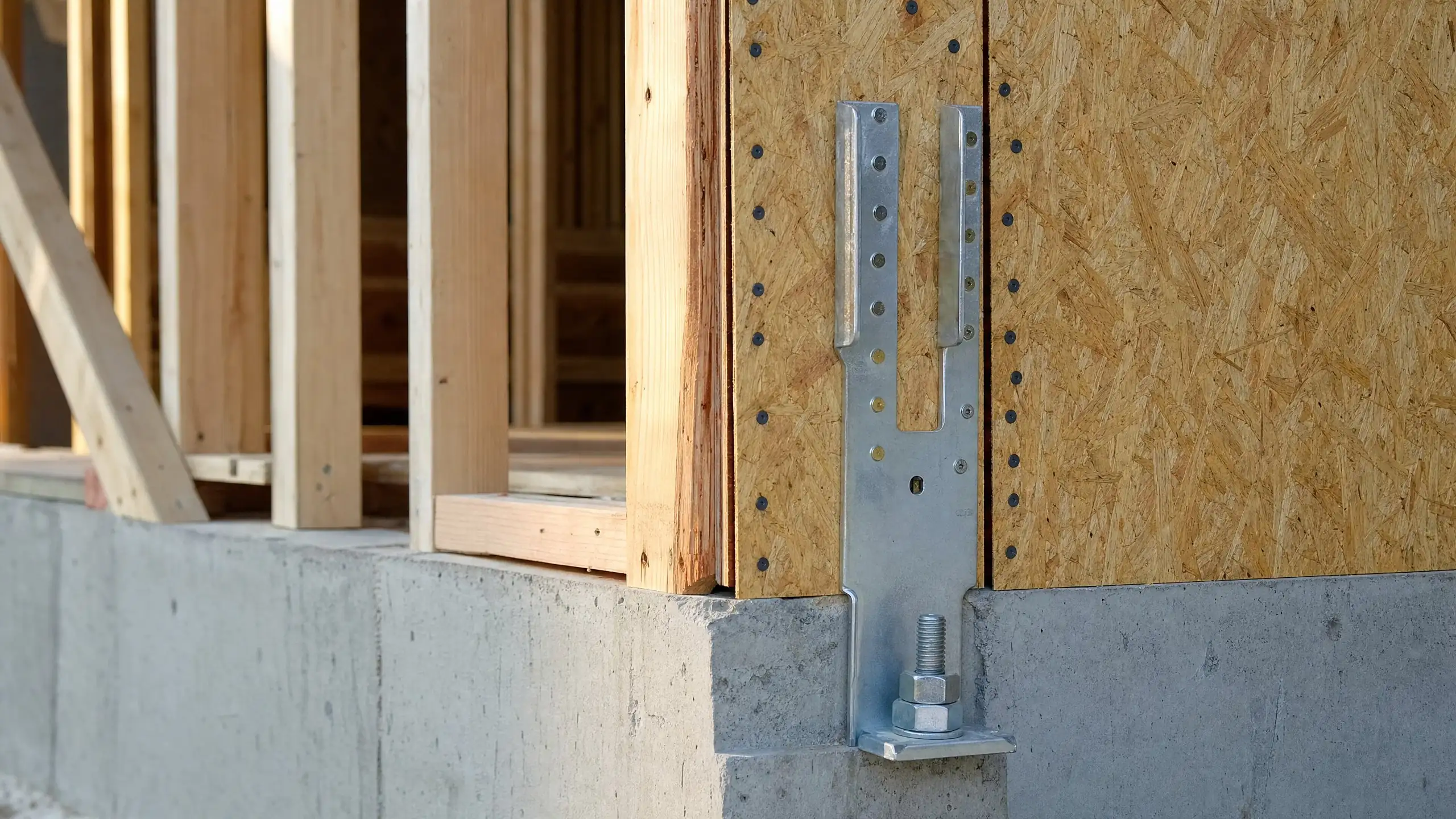 Steel hold-down connector and anchor bolt on a plywood shear wall in new addition framing