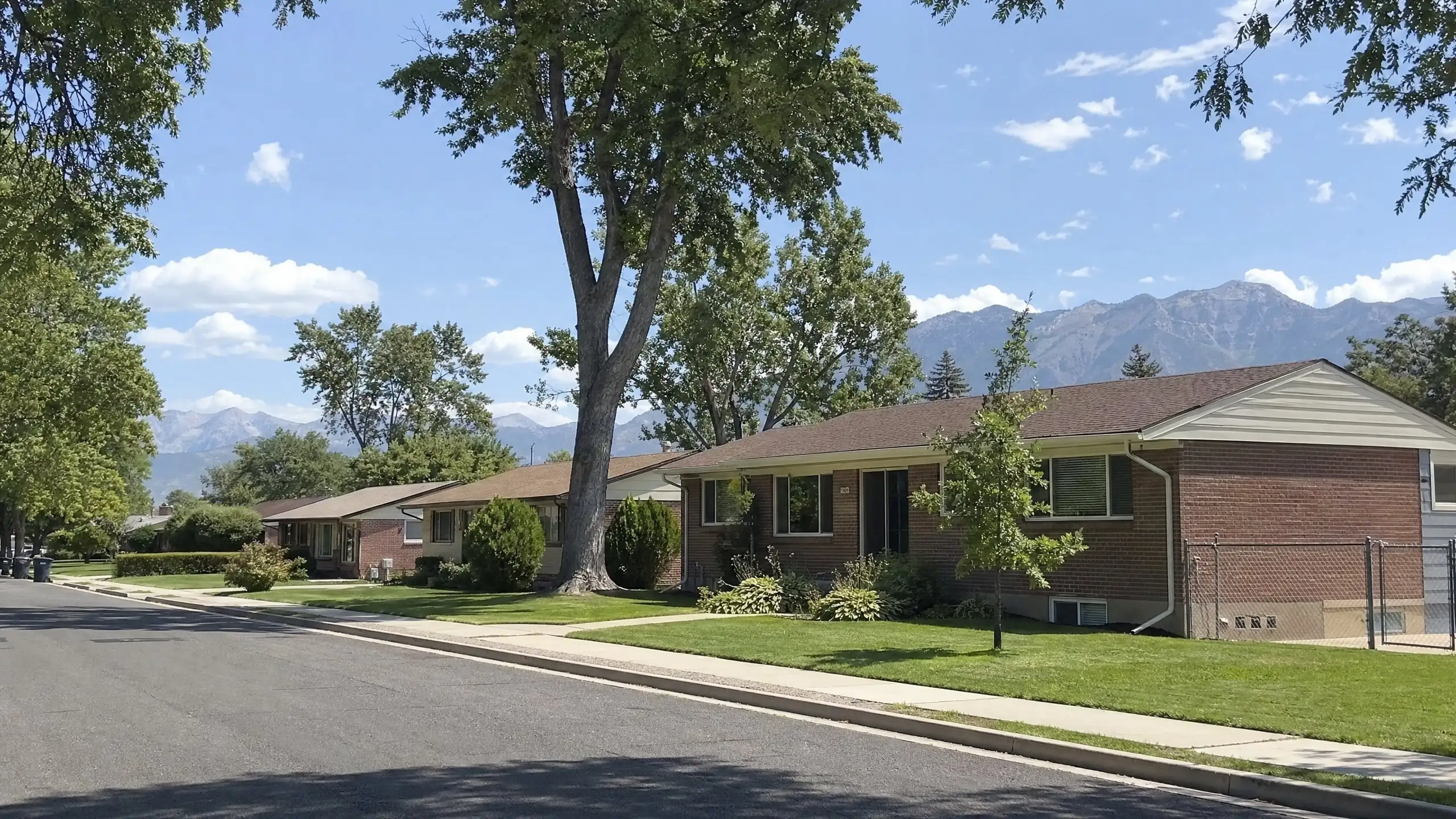 Level street of brick ramblers under mature shade trees, one with a matching rear addition