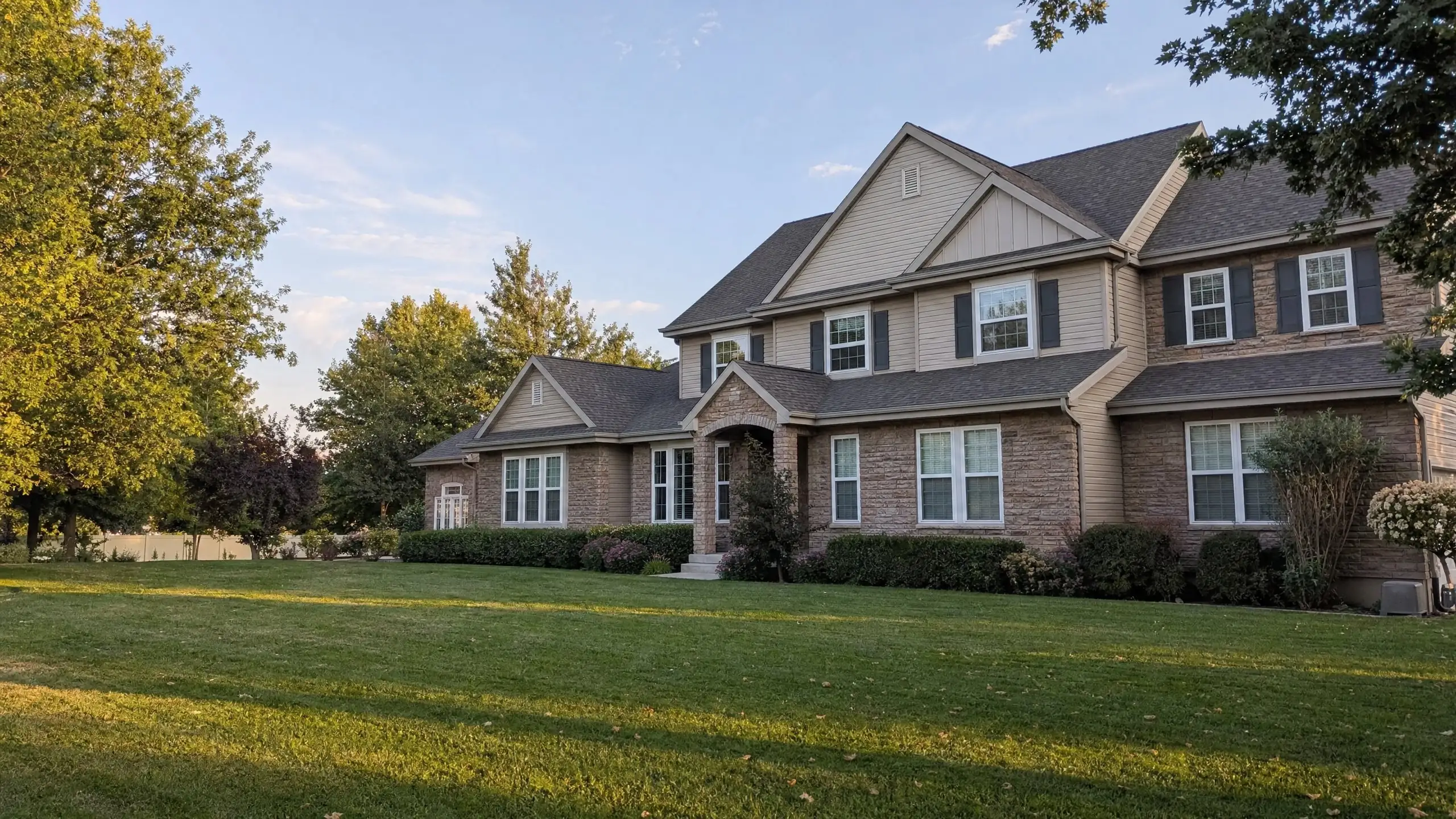 Large family home with a main-floor wing and second-story addition in matching stone and siding