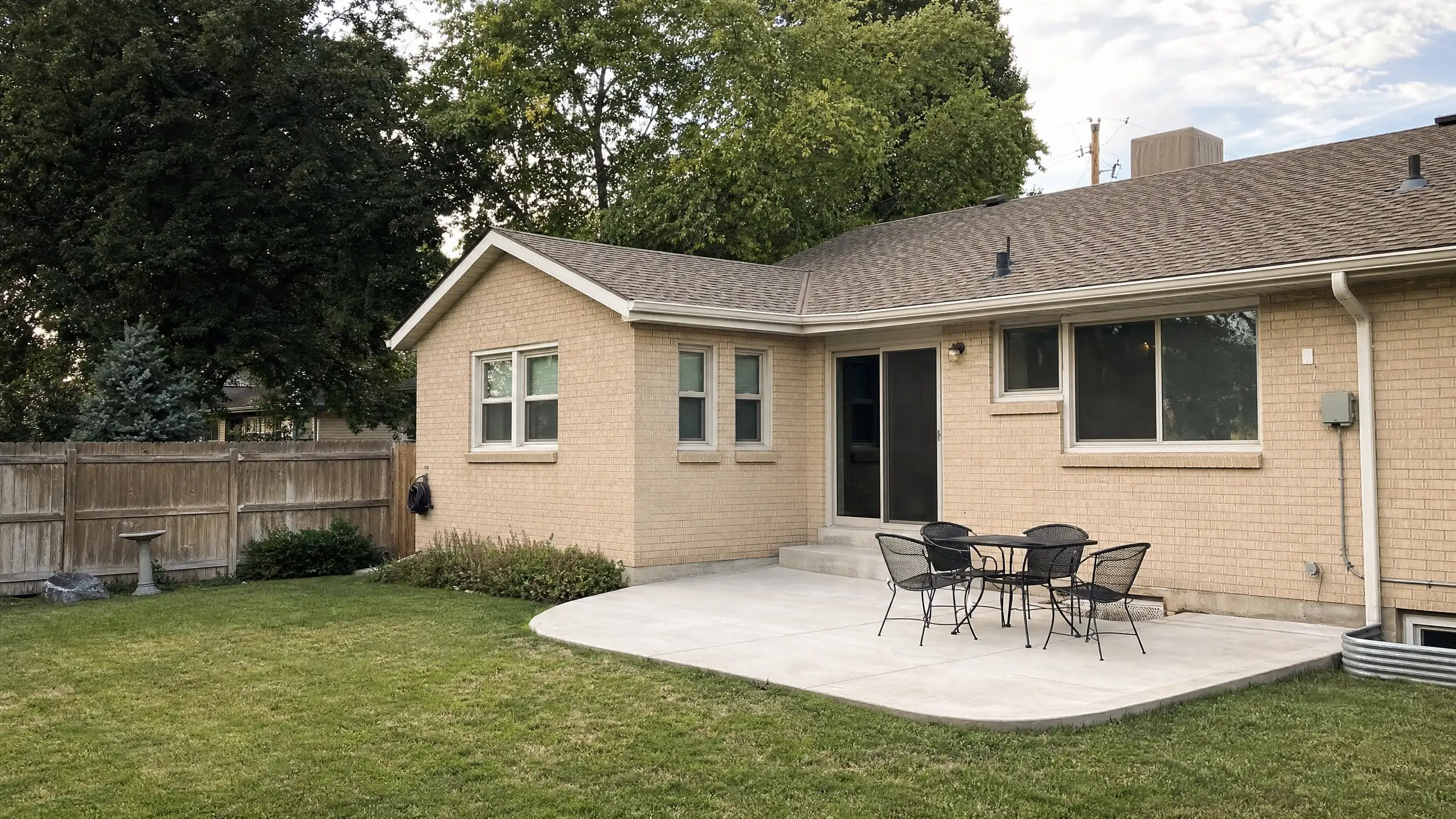 Backyard of a rambler with a modest rear addition beside a concrete patio and privacy fence