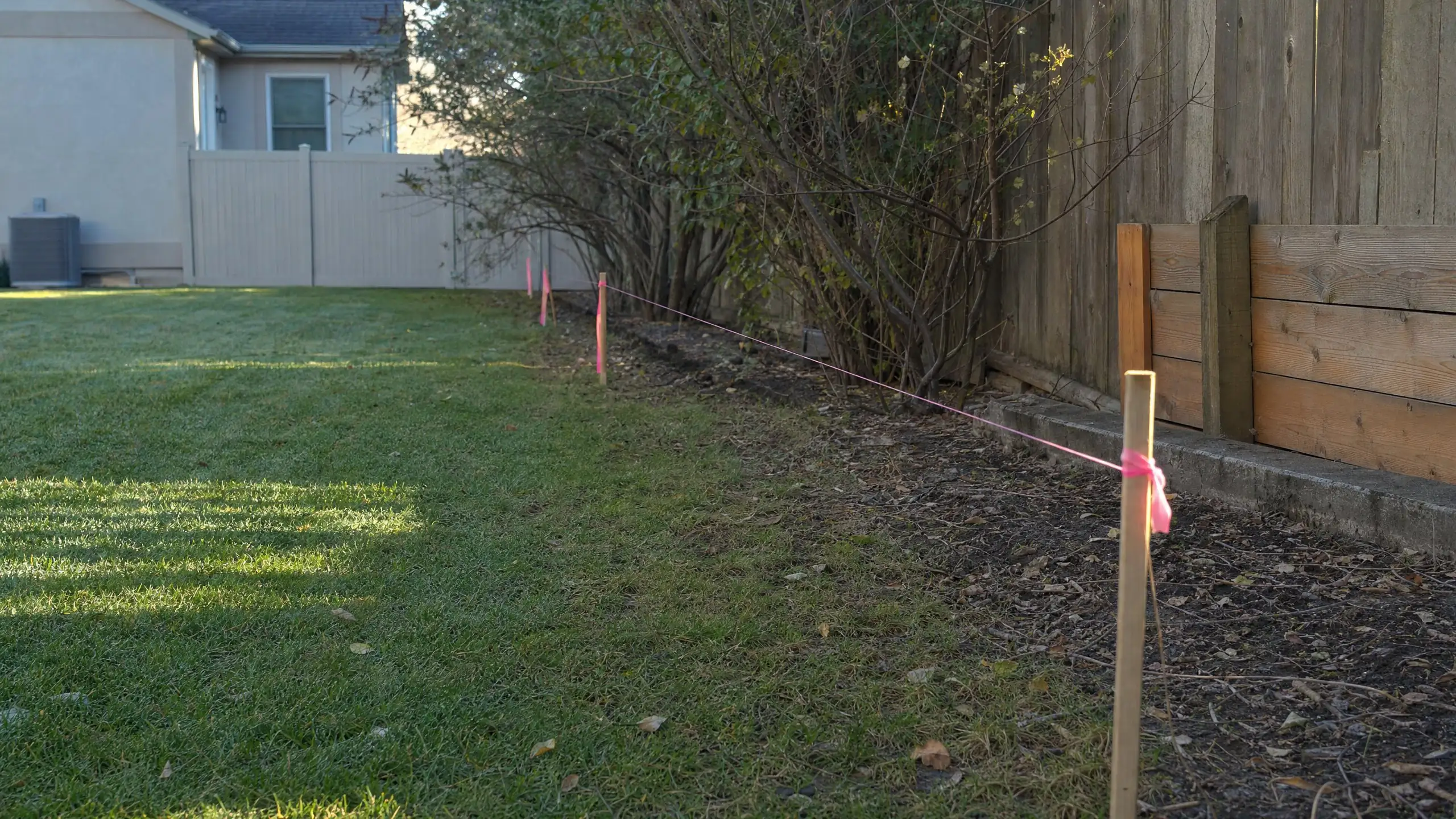 Survey stakes with pink flagging and a string line marking a property line beside a home